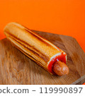 Grilled hot dog wrapped in toasted bread with ketchup on a wooden surface against an orange background. Studio food photography. Fast food and snack concept. Design for poster, banner, menu, wallpaper 119990897