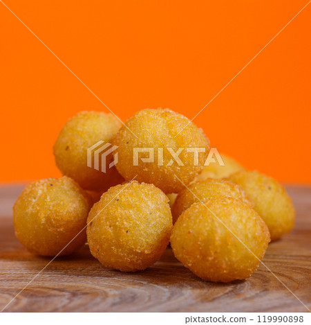 Pile of crispy breaded potato balls on a wooden surface against an orange background. Studio food photography. Snack and appetizer concept. Design for poster, banner, menu, wallpaper 119990898