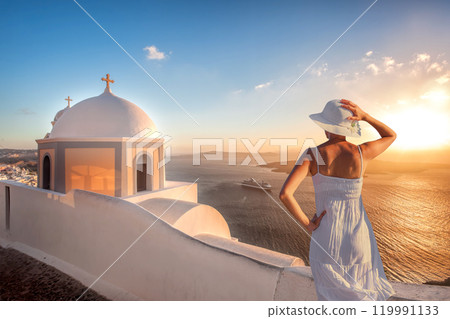 Beautiful young woman enjoying the sunset view of Thira town with church on Santorini island in Greece 119991133