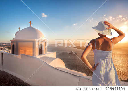 Beautiful young woman enjoying the sunset view of Thira town with church on Santorini island in Greece Beautiful young woman enjoying the sunset view of Thira town with church on Santorini island in Greece 119991134