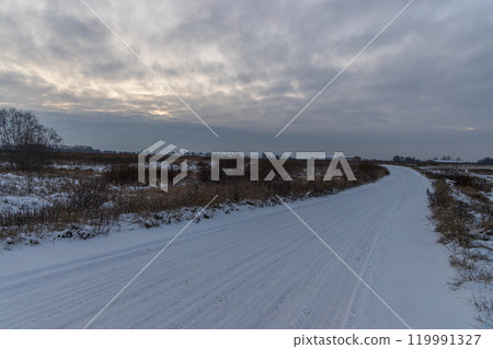 Winter landscape with sunset sky and empty snowy road. 119991327