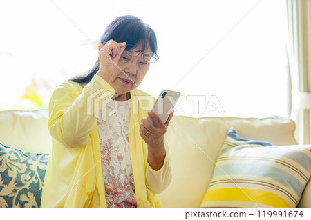 Senior woman looking at her smartphone while shifting her reading glasses 119991674