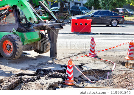 Construction work in progress on a city street with machinery and safety barriers in bright sunlight 119991845