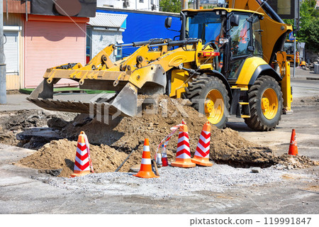 Construction workers using heavy machinery to repair urban road during daytime 119991847
