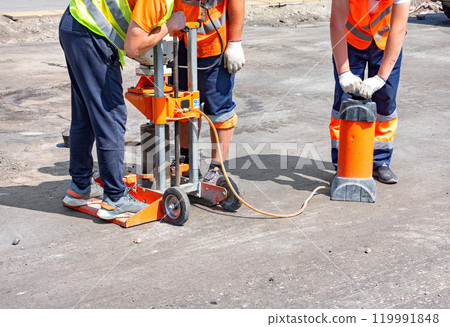 Construction workers drilling pavement on a sunny day at a busy urban site 119991848