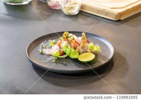 Spicy Raw Salmon Salad Thai food style decorated with Crispy fried fish skin and Yellow Flower on top and micro herb around dish. Ready to serve and eat. 119991895
