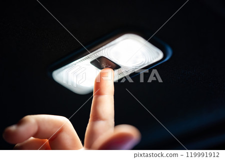 Close up a small finger from little 5 years old girl raises hand up to turn on and turn off car lamp at the back seat ceiling inside the car. 119991912