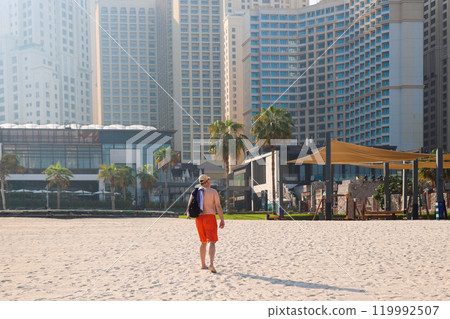 A large adult man returns to a city hotel after relaxing on the beach. View from the back 119992507