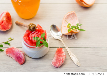 homemade sweet yogurt in a glass jar with pieces of red ripe grapefruit and honey, on a wooden table 119992541