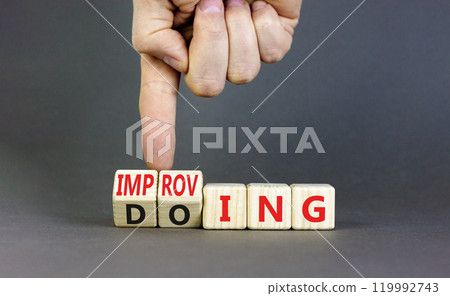 Doing or improving symbol. Businessman turns wooden cubes and changes the word Doing to Improving. Beautiful grey table grey background. Educational business doing or improving concept. Copy space 119992743