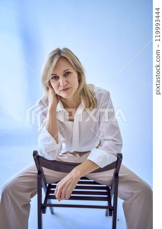 portrait of a stylish blonde middle-aged woman in a white blouse and beige pants portrait of a stylish blonde middle-aged woman in a white blouse and beige pants 119993444