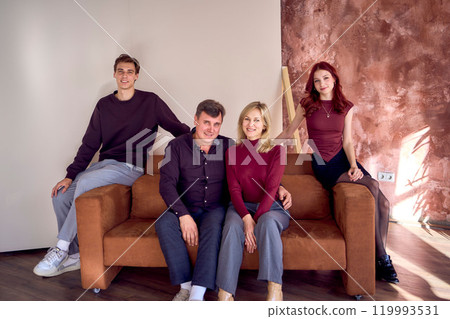 family, middle-aged husband and wife, young son and teenage daughter, sitting on sofa, studio photo shoot 119993531