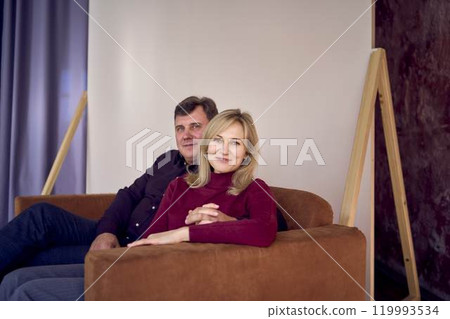attractive middle-aged married couple hugging and smiling on sofa, studio photo shoot attractive middle-aged married couple hugging and smiling on sofa, studio photo shoot 119993534