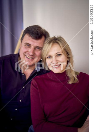 attractive middle-aged married couple hugging and smiling on sofa, studio photo shoot attractive middle-aged married couple hugging and smiling on sofa, studio photo shoot 119993535