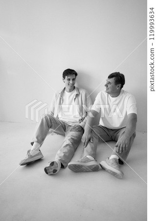 a     portrait of a middle-aged man  and his adult son sitting by the wall on a white background 119993634