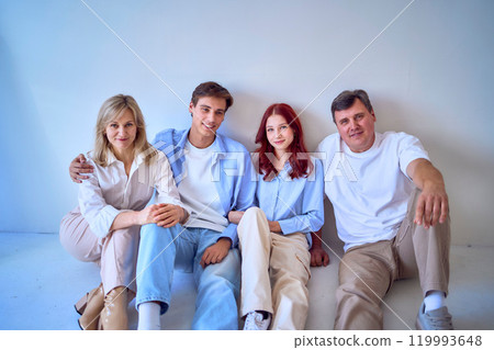 a family, middle-aged husband and wife, young adult son and teenage daughter, sitting on a white background, studio photo shoot 119993648