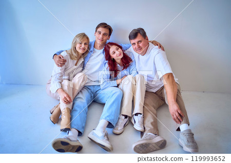 a family, middle-aged husband and wife, young adult son and teenage daughter, sitting on a white background, studio photo shoot 119993652
