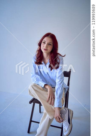 portrait of a beautiful teenage girl with red hair sitting on a chair on a white background 119993689