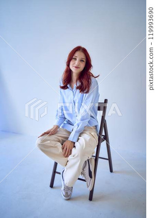 portrait of a beautiful teenage girl with red hair sitting on a chair on a white background 119993690