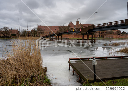 A bridge over the Nogat river with the Castle of the Teutonic Order in Malbork in the background. This is the largest castle in the world measured by land area and a UNESCO World Heritage Site 119994022