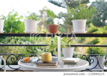 Laptop side view and yellow coffee cup with notebooks on white metal table outdoor balcony 119994225