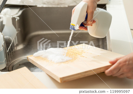 The hands of a middle-aged to senior woman bleaching and disinfecting a cutting board 119995097