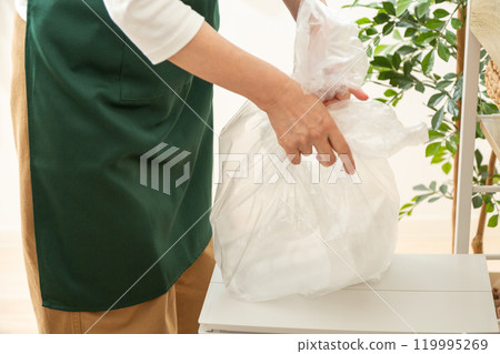 The hands of middle-aged to senior women sorting and throwing away recyclable waste 119995269