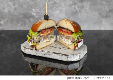 Burger on a wooden board with a patty, tomato, cheese, cucumber and lettuce. Burger on a wooden board with a patty, tomato, cheese, cucumber and lettuce. 119995454