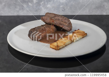 Baked beef with chocolate-wine sauce and croutons. Meat on a white plate. 119995458