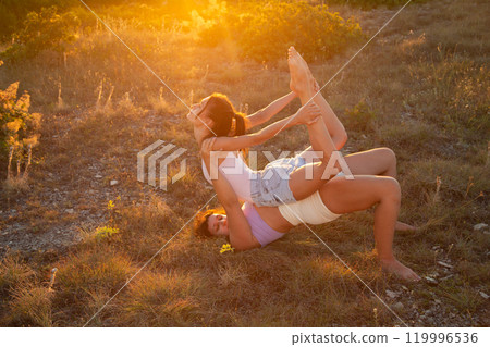 Young women gymnasts training in bright rays of sunset. Fly yoga Young women gymnasts training in bright rays of sunset. Fly yoga 119996536