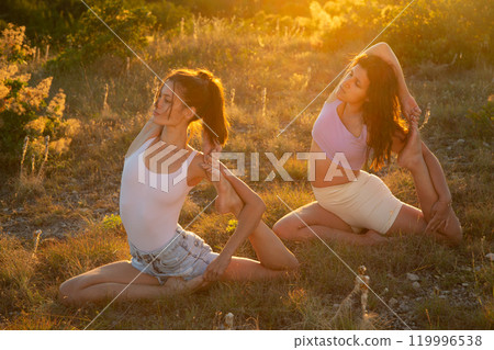 Young beautiful women gymnasts doing yoga on the grass against the sunset 119996538