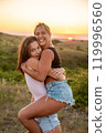 A joyful meeting of girlfriends with hugs against the backdrop of the sunset. Vertical composition 119996560
