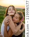 Vertical composition. Young beautiful women happily hugging against the sunset 119996577