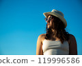 Portrait in profile of young woman in white dress and sunglasses with hat posing against the backdrop of sky 119996586