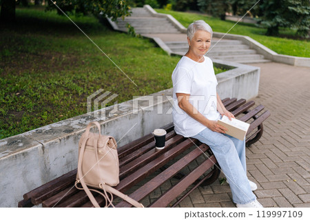 Portrait of relaxed senior woman finding peace and wisdom in retirement as reads in tranquil park, surrounded by nature on summer day. Aged female with short gray hair enjoying free time in retirement Portrait of relaxed senior woman finding peace and wisdom in retirement as reads in tranquil park, surrounded by nature on summer day. Aged female with short gray hair enjoying free time in retirement 119997109
