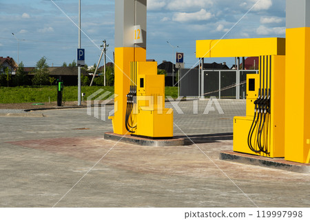 A bright, modern fuel station features yellow pumps set in a spacious, open area under a clear blue sky. Nearby parking spaces are visible, enhancing accessibility 119997998