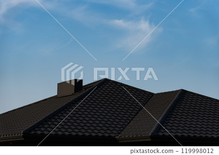 The roof of a suburban house is visible against a bright blue sky with wispy clouds. The textured tiles create a distinct pattern, enhancing the architectural features 119998012