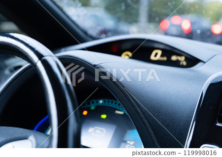 The dashboard displays various vehicle functions, including speed and fuel, as the rain obscures visibility while driving through heavy city traffic 119998016