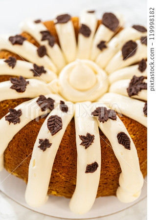 Icing the pumpkin bundt cake with cream cheese frosting and decorating it with chocolate leaves. 119998182