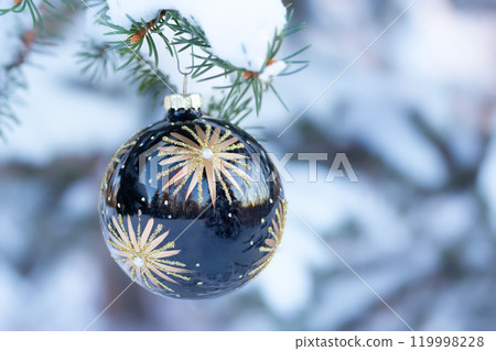 Black Christmas ball with golden stars is on a snowy branch. Black Christmas ball with golden stars is on a snowy branch. 119998228