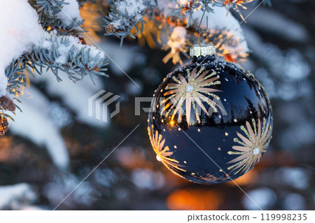 Navy blue Christmas decoration is on the snowy branch in sunset. 119998235