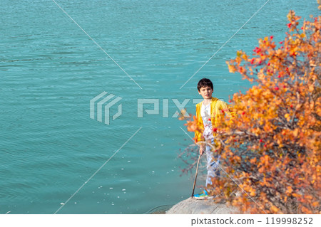 Teenage boy is enjoying a sunny fall day and the turquoise waters of the mountain river on his hike. Yellow foliage. 119998252
