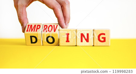 Doing or improving symbol. Businessman turns wooden cubes and changes the word Doing to Improving. Beautiful yellow table white background. Educational business doing or improving concept. Copy space 119998283