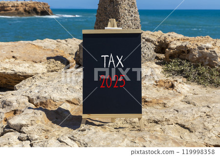 Planning tax 2025 new year symbol. Concept words Tax 2025 on beautiful yellow chalk blackboard. Beautiful stone beach blue sky sea background. Business tax 2025 new year concept. Copy space. 119998358