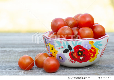 Red cherry tomatoes in a bowl with floral pattern. 119998432