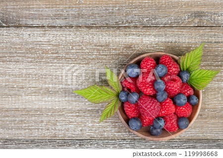 Plate with raspberries and blueberries with leaves on the wooden rustic table. 119998668