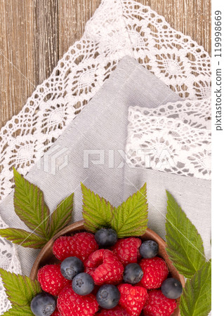 Plate with raspberries and blueberries on the wooden table with laced cloth. 119998669