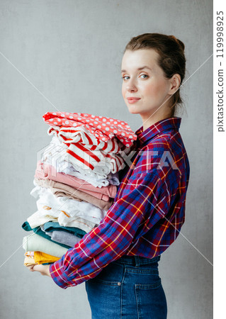 Housewife girl holds stack of clean clothes in hands after washing, drying. Housewife girl holds stack of clean clothes in hands after washing, drying. 119998925