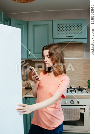 young woman looks into refrigerator in kitchen, orders food from delivery service, restaurant. 119998945
