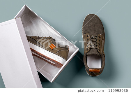 Khaki canvas sneakers in a box against silver blue background. Khaki canvas sneakers in a box against silver blue background. 119998986